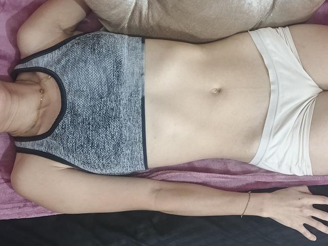 LilyHottie69's flat stomach with a small navel, wearing a gray sports bra and white panties, lying on a pink towel, arms resting, visible hand with a bracelet.