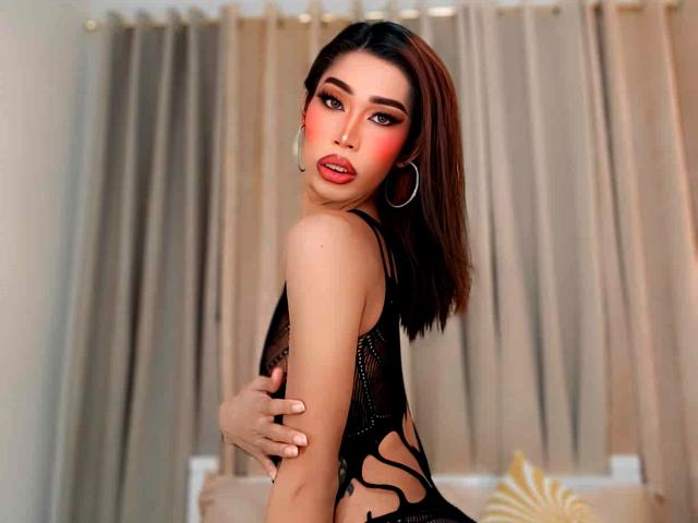 SeductiveBigCockSofia with red makeup, black lace top, hoop earrings, and brown bob, covering her tits with one hand, looking back with red lipstick.