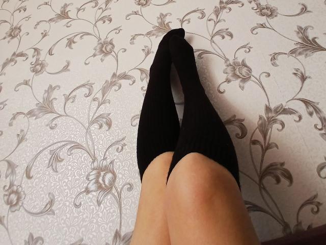 Diene's legs in black thigh-high socks, knees together, on a floral-patterned floor. Her skin is light and smooth. The socks are tight, covering her ass.