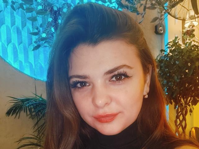 CherryMagdalena ha la pelle chiara, i capelli lunghi castani e indossa un eyeliner nero con ciglia lunghe. Le sue labbra rosa sono leggermente dischiuse. Sta guardando la fotocamera con un sorriso appena accennato..