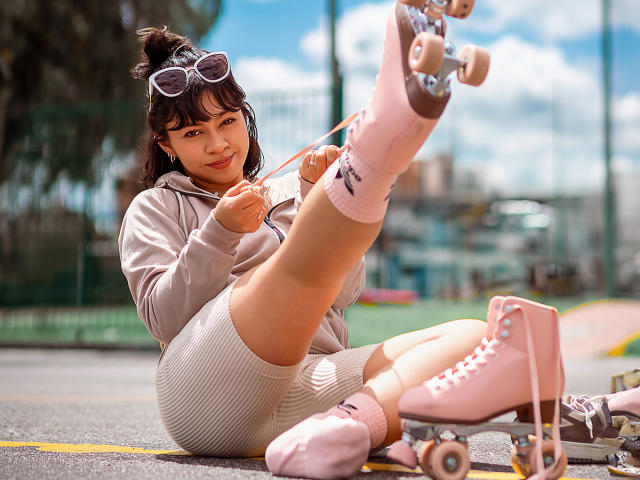 JuliettaHott with pink roller skates, grey hoodie, white shorts, and socks, adjusting her skates while sitting on a skatepark, showing her ass and cute face.