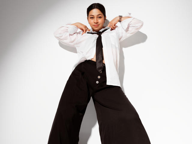 JuliettaHott, wearing a white shirt and black tie, with black pants, standing with legs apart, hands near her neck, looking down, showing her small tits and confident ass.