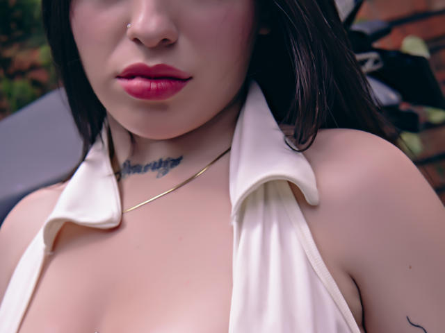 SteffaCandleX with red lipstick, white halter top, small gold necklace, tattoo on throat, and visible cleavage. Her skin is pale, and she has dark, straight hair.