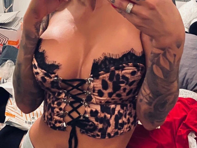 AlphaMaedchen-hot with tattoos, wearing a leopard-print lace-up corset, exposing her big, round, and perky tits, holding her hands near her face, showing a ring.