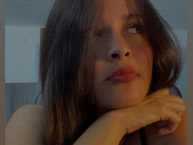 Gabrielafoxxy's face with brown hair, red lips, and a thoughtful expression, her hand resting on her chin, soft light, slight grainy texture, looking to the right.