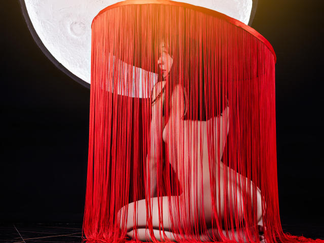 MillaHottLove69 crouches naked under a red curtain, her tits and pussy partially visible, with a large moon in the background, looking sexy and mysterious.