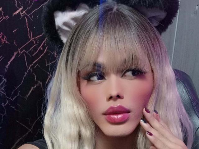 HottAntonella with blonde hair, cat ears, and pink glossy lips, looking to the side with heavy eyeliner and pink blush, hand near face, nails painted dark.