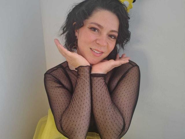 Daisy: Con i suoi capelli neri ricci, indossa una maglietta trasparente a pois neri e un vestito giallo, sorridendo e appoggiando il mento sulle mani. Ha degli orecchini carini e un'espressione giocosa..