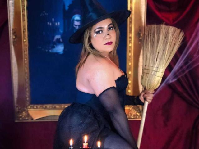 JadeSexiest with blonde hair, witch hat, black dress, and stockings, holding a broom, sitting with candles, sexy ass, and a confident, sultry expression, in a dark, magical setting.