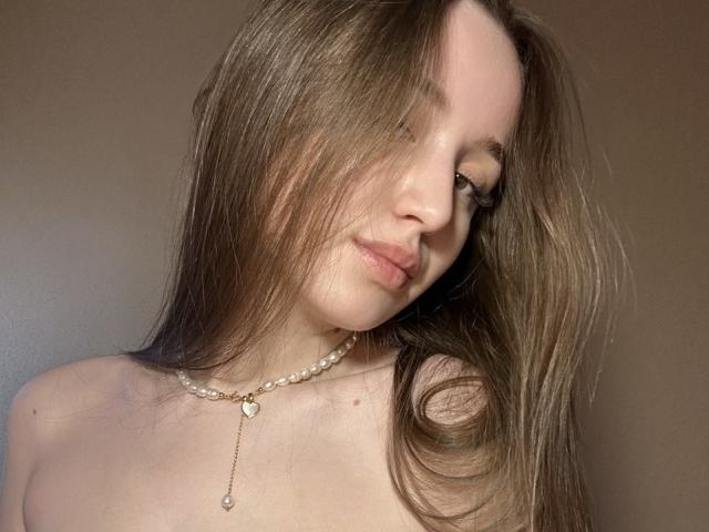 LeslieBer with long brown hair, light skin, and a pearl necklace, has her tits slightly visible, and a subtle, sexy smile, with her hair covering one eye.
