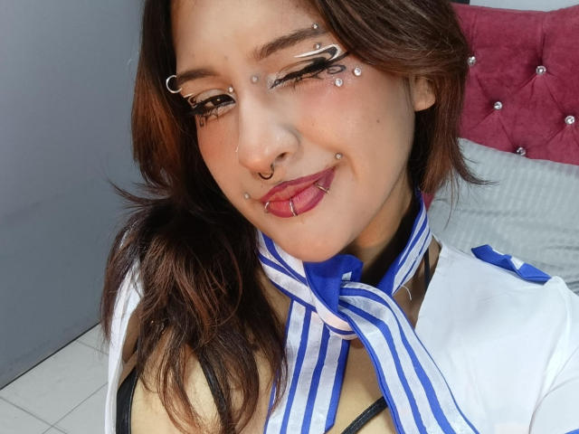 DanniLuke ha i capelli castani, diversi piercing sul viso e una sciarpa a righe blu e bianche. Indossa una camicia bianca, con la lingua fuori, mostrando il suo piercing rosa sulla lingua..