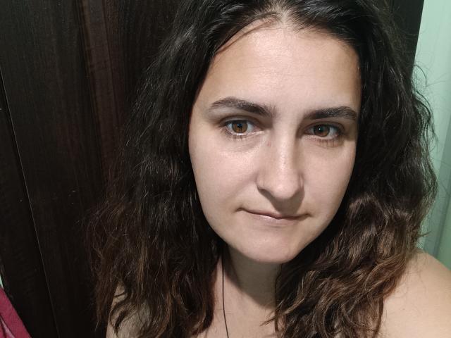 KotovamalaHot has wavy brown hair, brown eyes, and a slight smile with a small nose and thin eyebrows. She's wearing a necklace and has a pale skin tone.