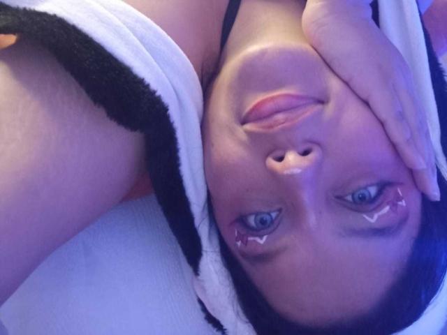KonyBella's face is upside down, with her hand over her cheek, blue eyes, and black and white striped shirt, showing red eyeliner. Her tits are partially visible.