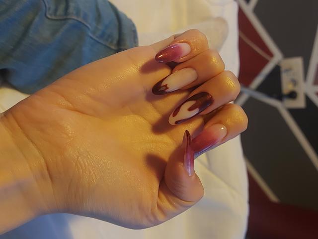 Les mains de JuliaHuntis, avec ses ongles blancs et marron ornés de pointes rouge foncé brillantes, sont visibles, tout comme sa poitrine lisse et bien entretenue, exposée sur une serviette blanche, à côté d'un vêtement en jean bleu..