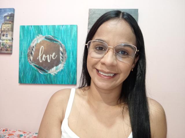 YisethLucia has long black hair, wears glasses, and smiles showing teeth. She's in a white tank top with her tits barely visible. Her pussy is not shown.
