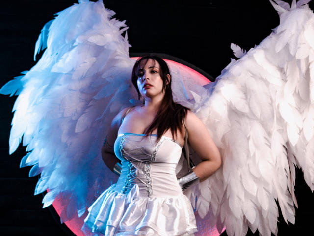 Rosalinnes with big white angel wings, wearing a tight white strapless dress, corset, and white gloves, has long dark hair, and a curvy, busty, pale-skinned body.