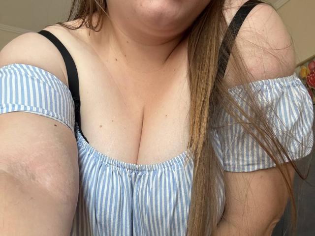 Leiliia's tits are visible in a blue and white striped off-shoulder top, showing her black bra straps and long brown hair, with a slight view of her chin.
