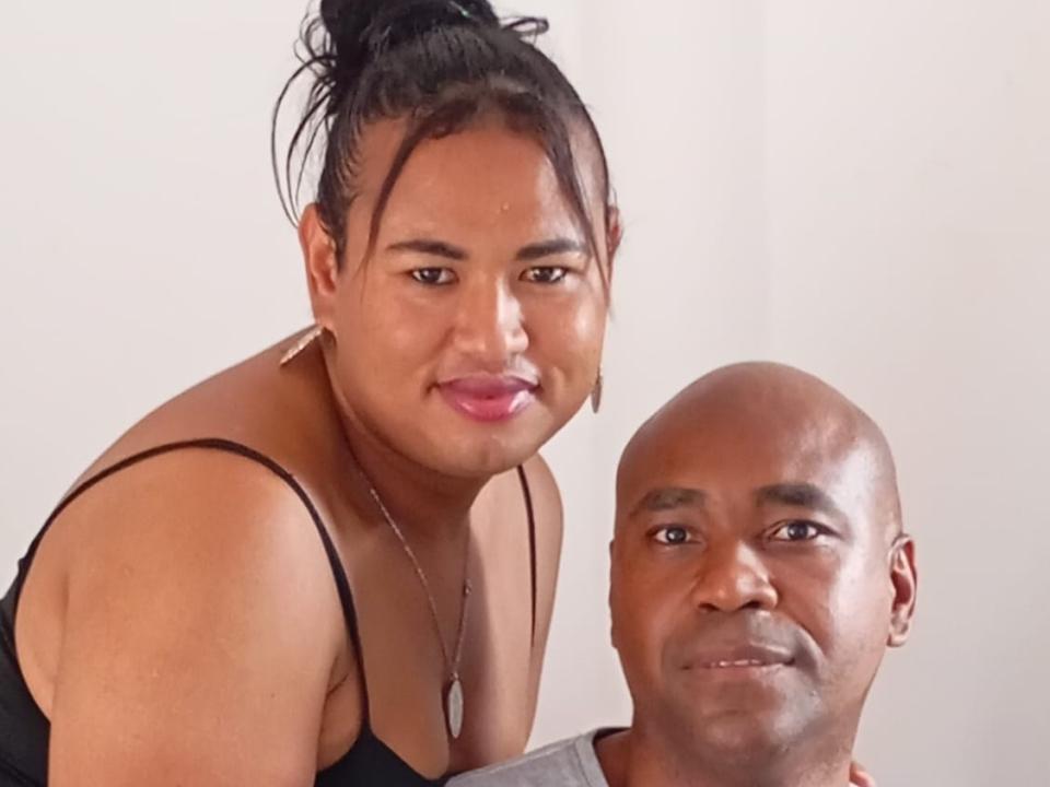 MichaelYJoselyn with big tits leaning over a bald dude with a small nose, both smiling at the camera. She's wearing a black top, he's in a gray shirt.