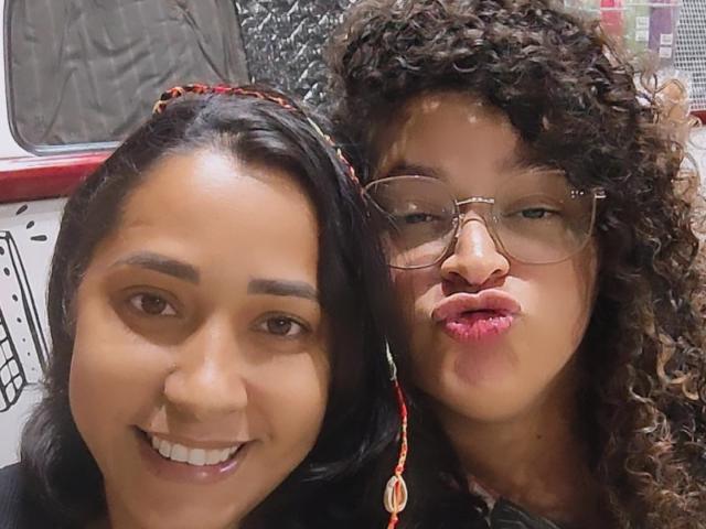 Marinomade with black hair and Marinomade with curly brown hair, wearing glasses, puckering lips, both smiling. Marinomade on left has straight hair, Marinomade on right has curly hair.
