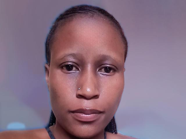 LisaLena's face with dark brown skin, small nose piercing, shiny lips, and subtle makeup, looking straight at the camera, with braided hair and a neutral expression.