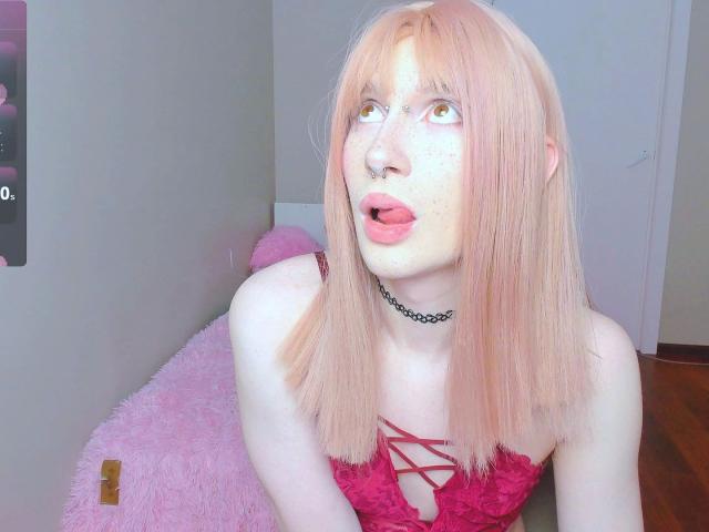 Mika-Candy-hot with pale pink hair, freckles, and a nose ring, wearing a red lace-up top, tongue out, and a black choker, looking up with yellow eyes.
