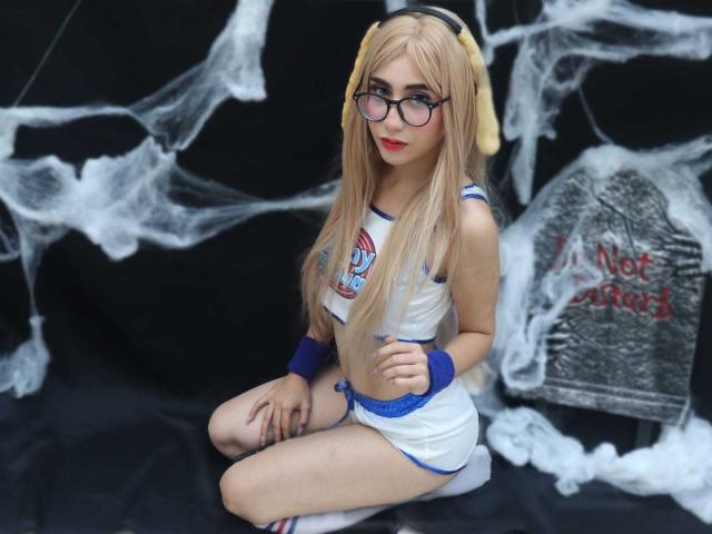 DinnyPink with long blonde hair, glasses, and dog ears, wearing a white and blue sports outfit, sitting on a black surface, showing her ass and small tits.