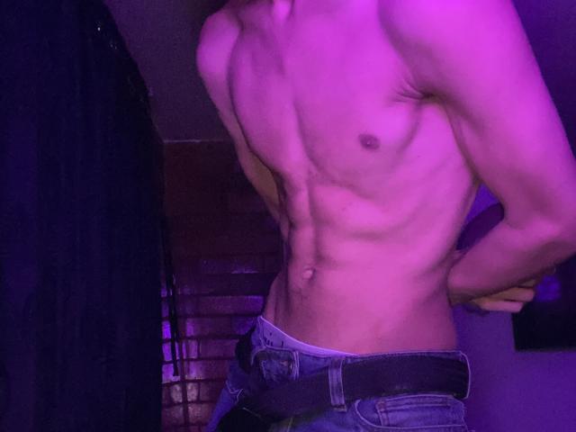 Angelitocute's shirtless, muscular, toned body with visible abs, small nipples, and jeans with a belt, all under purple lighting. Hands are behind Angelitocute's back.