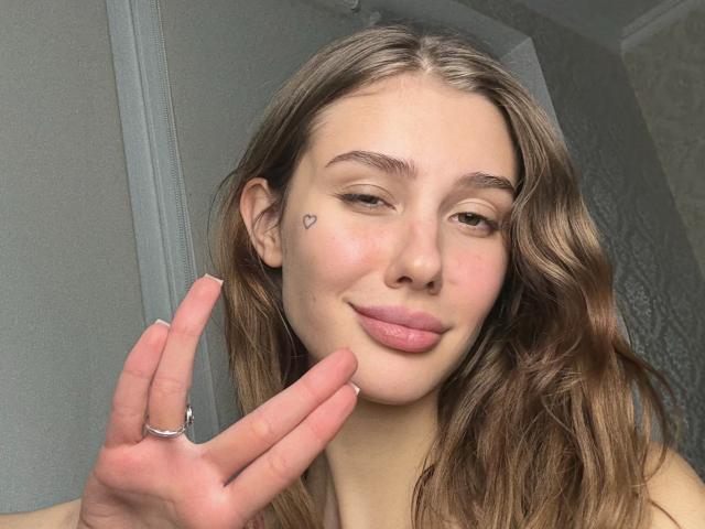 SensualMila a les cheveux bruns ondulés, un petit tatouage en forme de cœur sur sa joue droite, et des lèvres roses brillantes. Elle fait un signe de la paix avec sa main droite et porte une bague en argent..