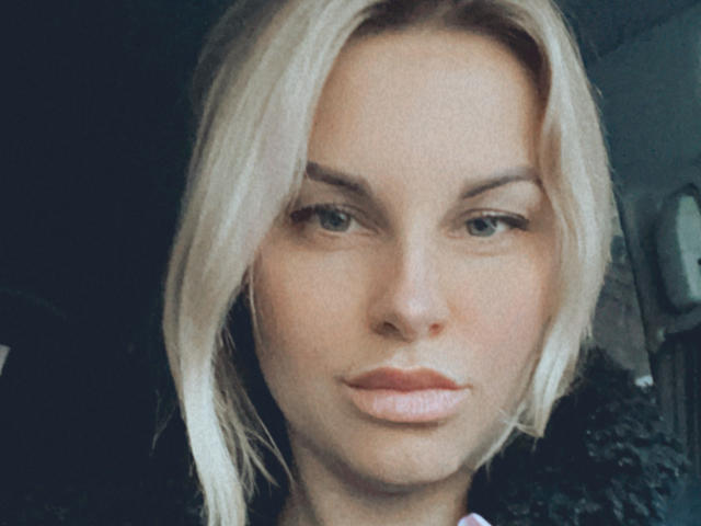 BelleLisaG has blonde hair, green eyes, and pinkish lips with a slightly serious expression. Her face is centered in the shot, looking directly at the camera.