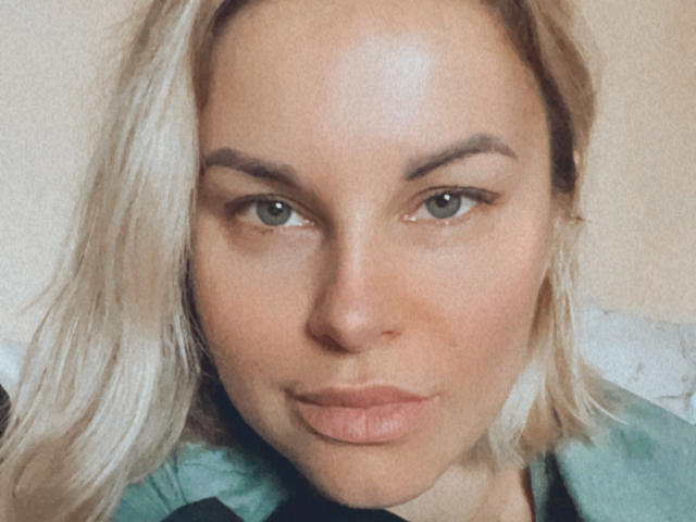 BelleLisaG's face, pale skin, blonde hair, green eyes, subtle makeup, pouty pink lips, green shirt, slightly messy hair, soft light, relaxed expression, subtle eyeliner, natural look.