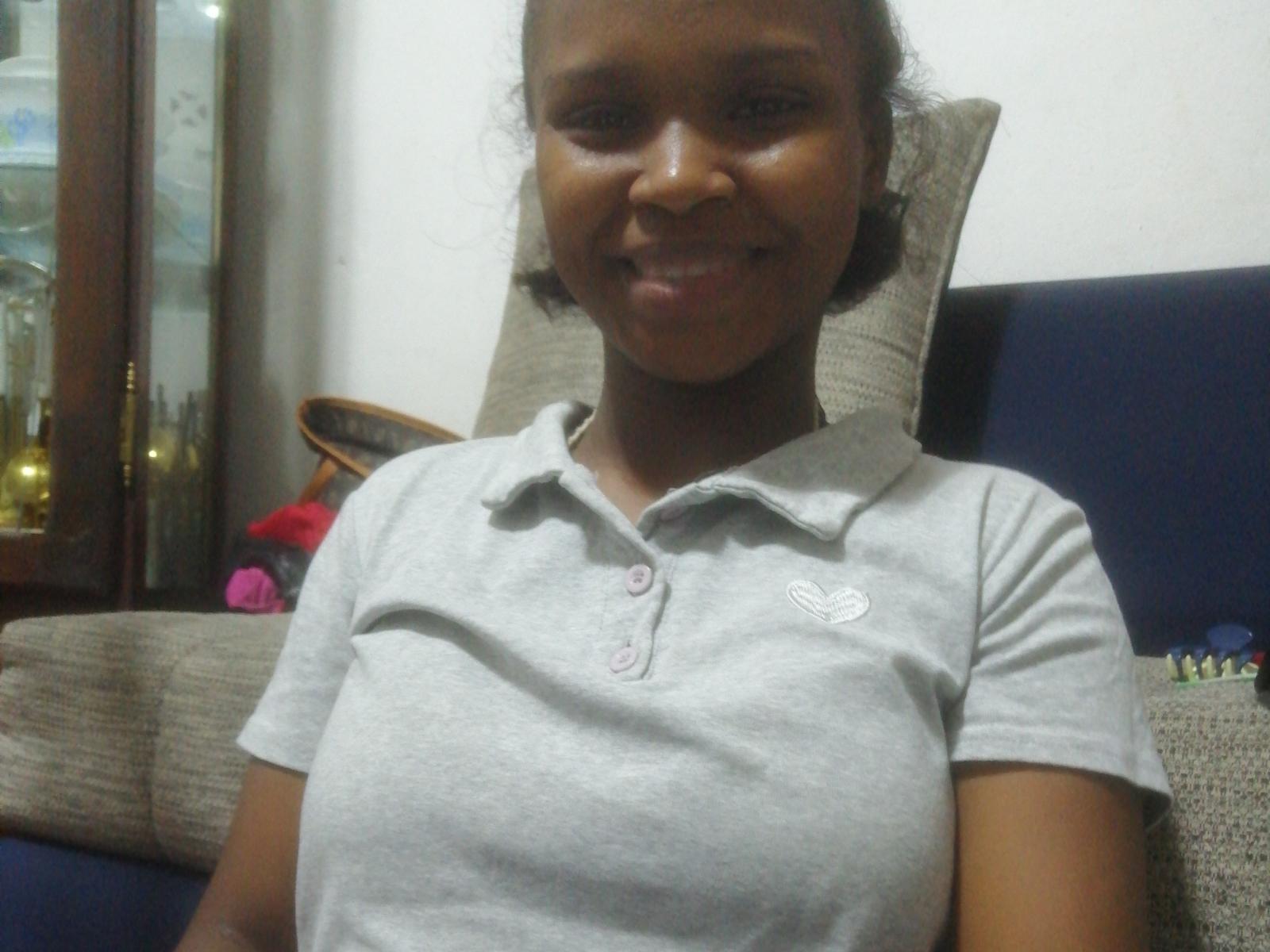 KittySxexy has dark brown skin, short curly hair, and wears a gray polo shirt with pink buttons, showing small tits, smiling with a relaxed, cute look.