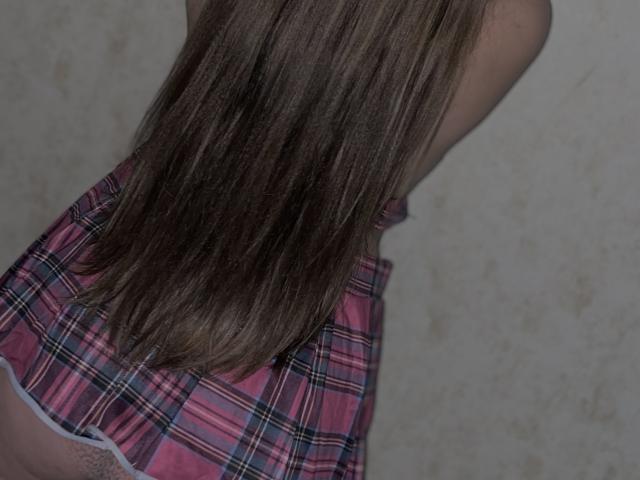 Madrinia's long brown hair, straight and shiny, covers her pink plaid skirt. Her back is to the camera, showing her upper body. Skirt is flared, pink with blue stripes.