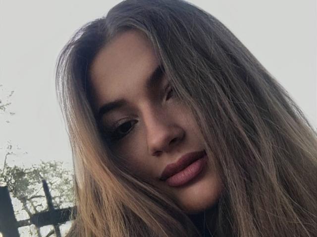 LeaHoty has long, straight brown hair, brown eyes, and pink lipstick. She's looking slightly to the side with a subtle, confident smile. Her nose is small and cute.