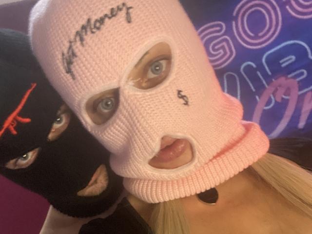 SinfulUnion wearing a pink knitted mask with "Kittensf" and "$" on it, black mask with red "X" over one eye, blonde hair, blue eyes, slightly open mouth.