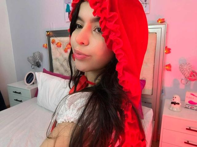 LissyCarter with long brown hair, red hooded dress, white lace top, red ribbon, pouty lips, soft pink bedroom, white bed, pink and orange decor, cute and sexy.
