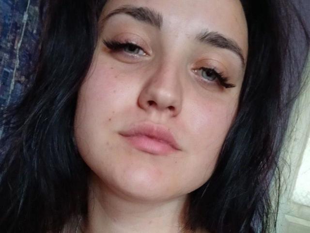 ScarletCargo has dark, wavy hair, thick eyebrows, long eyelashes, and a slightly pouty expression with pink lips. She's looking straight at the camera.