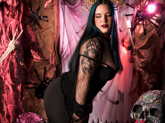 AuroraSantorini with blue hair, black lace sleeves, and black dress, bending forward, showing her ass, in a spooky, skull-filled, red-lit, crumpled-paper setting.