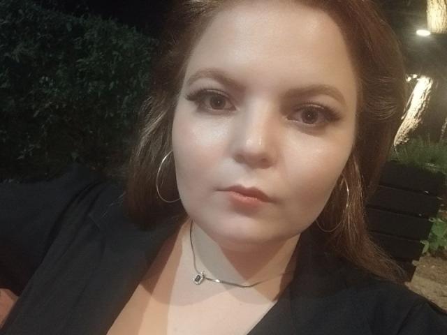 RenesmeeSunset has fair skin, brown eyes, and brown hair, wearing a black top with a necklace, and large silver hoop earrings, looking serious in a nighttime selfie.