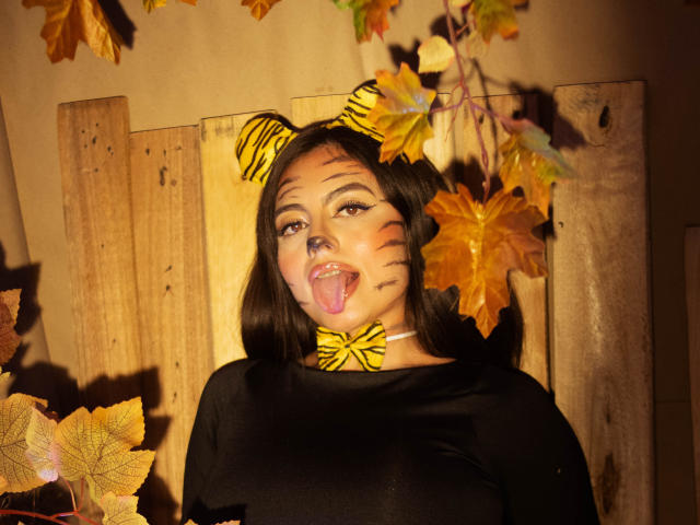DorothyLane con orecchie a forma di tigre e viso striato, top nero, lingua fuori, fiocco giallo a forma di foglia, recinzione di legno, foglie autunnali, luce calda, pelle media, capelli neri, carina, sexy..