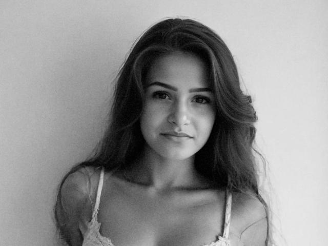 Black-and-white photo of LiaMia-hot with long, wavy hair, wearing a lace bra, showing her tits, and a subtle smile, against a plain background.