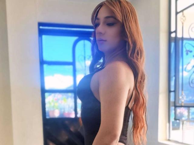 CatalineHot with long, wavy, red-orange hair, wearing a black, tight, sleeveless top, showing her bare, small-ass, and looking over her shoulder with a pouty expression.