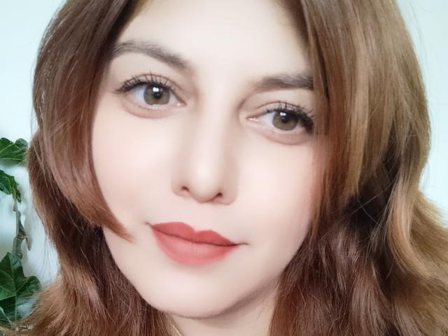 LoreyJolie has fair skin, brown eyes, and light brown wavy hair with red lipstick. Her small nose and full lips are visible. She looks cute and has a slight smile.
