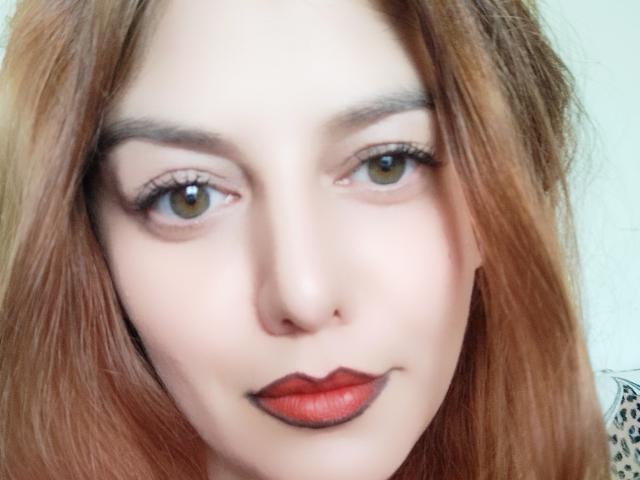 LoreyJolie's face with light brown eyes, red lipstick, and straight red-brown hair, slightly smiling, with thin eyebrows and subtle makeup.