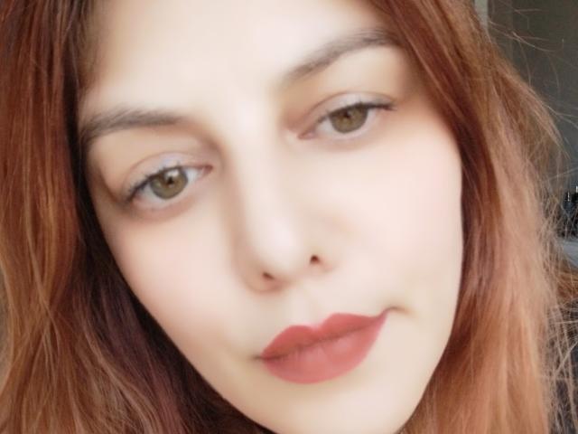LoreyJolie has fair skin, brown eyes, and reddish-brown wavy hair. She's wearing red lipstick and has a subtle smile, looking directly at the camera.
