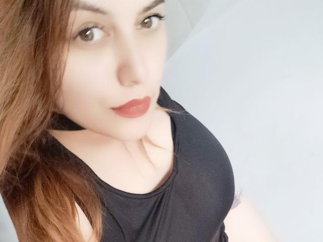 LoreyJolie with light skin, brown hair, red lipstick, and black sleeveless top, looking up at the camera, showing her chest.