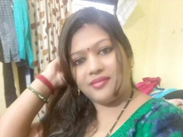 Nehaaahire-hot with long brown hair, green and blue patterned top, red lipstick, and a red bindi. She's smiling, hand in hair, wearing red and green bracelets.