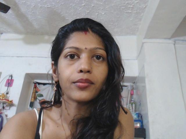 Nehaaahire-hot with medium brown skin, black wavy hair, red dot on forehead, nose ring, and hoop earrings, wearing a white strap, looking slightly to the side.