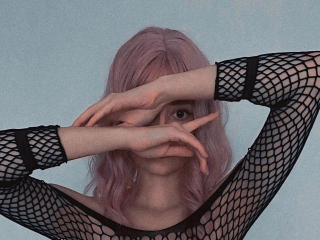 RushBonnie with pink hair, wearing a black fishnet top, covering her eyes with her hands, showing her nose and mouth, and her tits are slightly visible through the mesh.