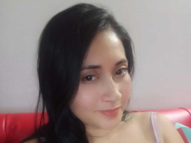 CatalinaGrey has black hair, brown eyes, and a slight smile. She's wearing a pink strap, and her tits are partially visible. Her skin is light.