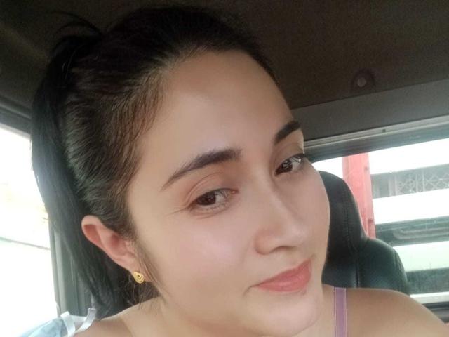 CatalinaGrey has light skin, dark eyebrows, and black hair in a ponytail. She's wearing a pink top and gold earrings, with a slight smile and pink lipstick.